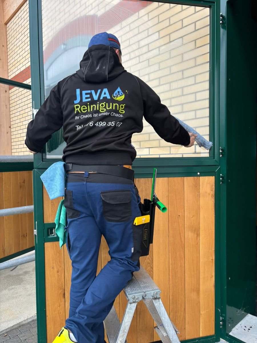 Mitarbeiter der Jeva Reinigung in Firmenkleidung reinigt von einer Leiter aus ein Wintergartenfenster